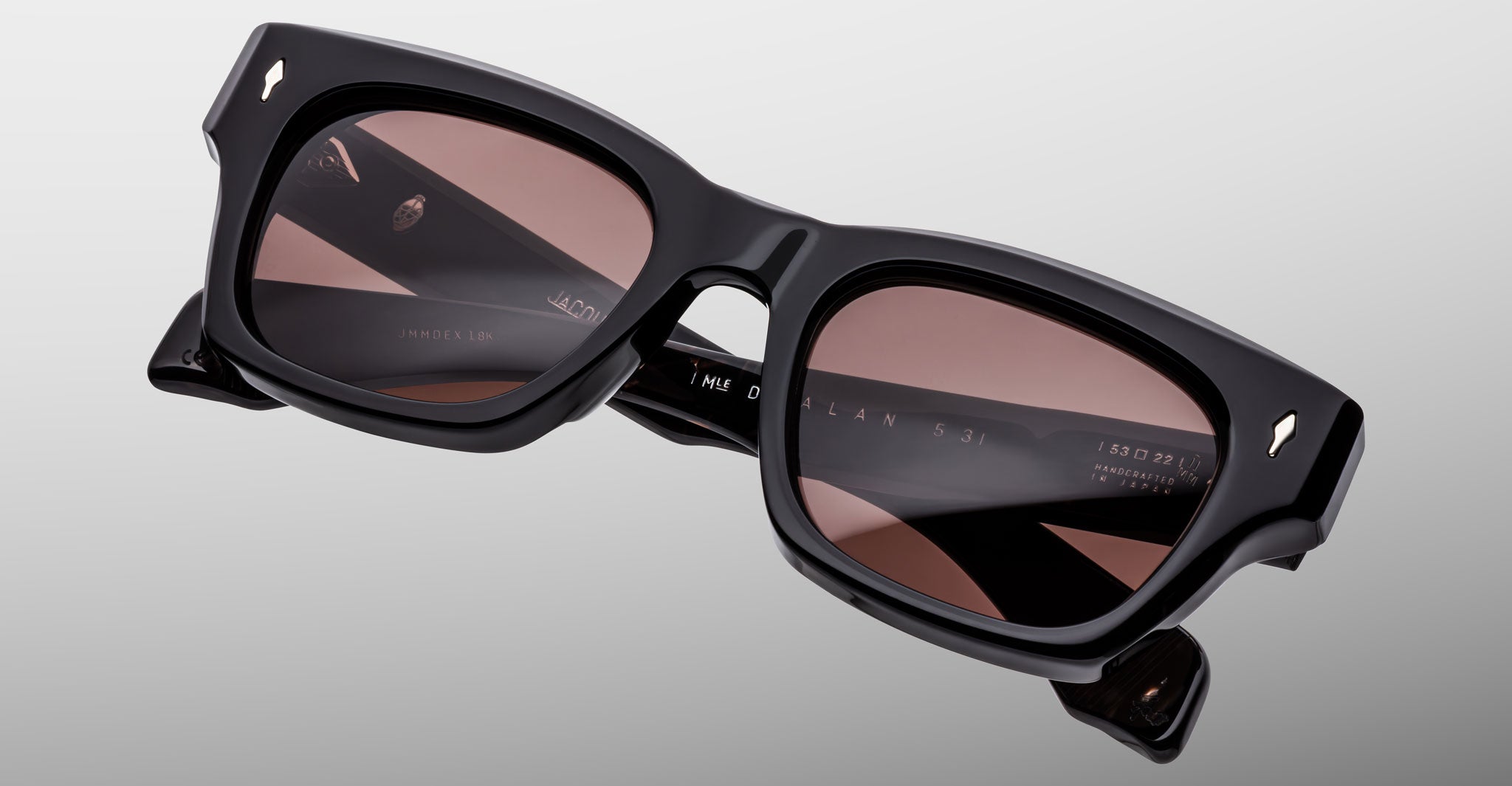 The Jacques Marie Mage Dealan 53 is a pair of black rectangular sunglasses with thick frames and dark tinted lenses, shown against a light gray background. Branding details and text appear on the inside of the arms.