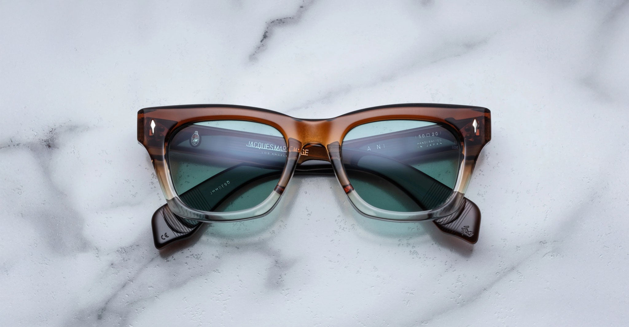 Jacques Marie Mage Dealan square eyeglasses with green lenses are shown from above on a flat surface.
