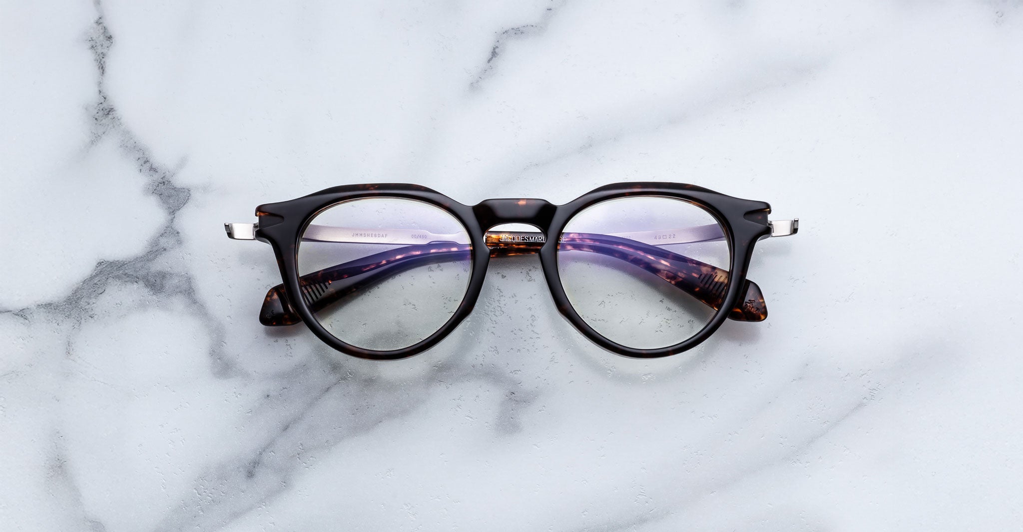 Jacques Marie Mage Desnos round dark tortoiseshell eyeglasses, top view, on white marble.