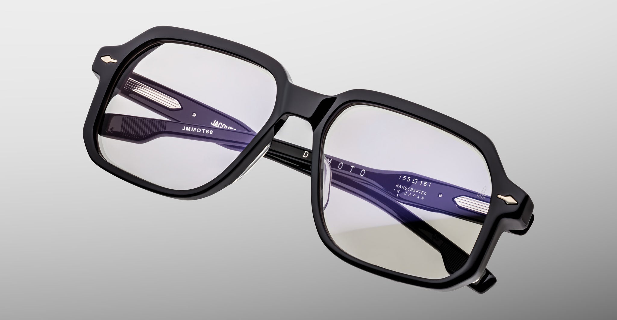 Jacques Marie Mage Domoto: Black rectangular eyeglasses with thick frames and metal corner accents, shown on a light gray background. Inner arms display white branding and details; handcrafted in Japan.