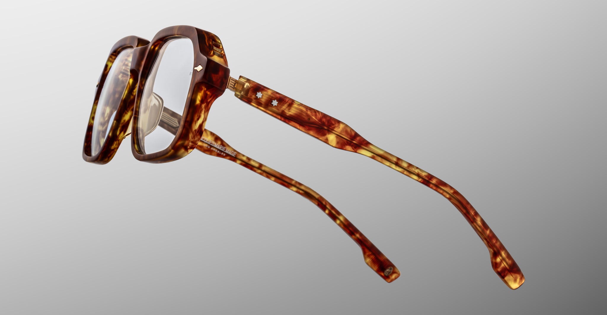 The Jacques Marie Mage Domoto is a pair of brown tortoiseshell eyeglasses handcrafted in Japan, featuring thick square frames and clear lenses, shown from a side angle against a plain gray background.