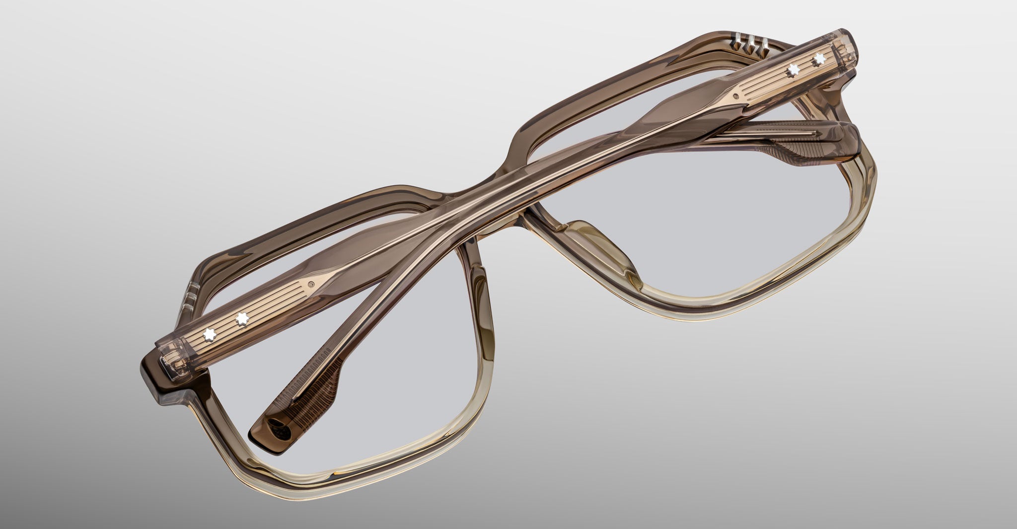 A pair of Jacques Marie Mage Domoto eyeglasses, featuring a stylish translucent brown geometric frame handcrafted in Japan, are folded and displayed on a gradient gray background.