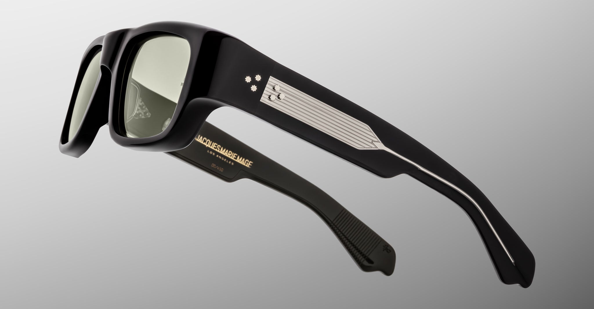 A close-up view of Jacques Marie Mage Donat black rectangular sunglasses with thick frames, metallic detailing, and a pattern of small dots on the temple arms, set against a plain light gray background.