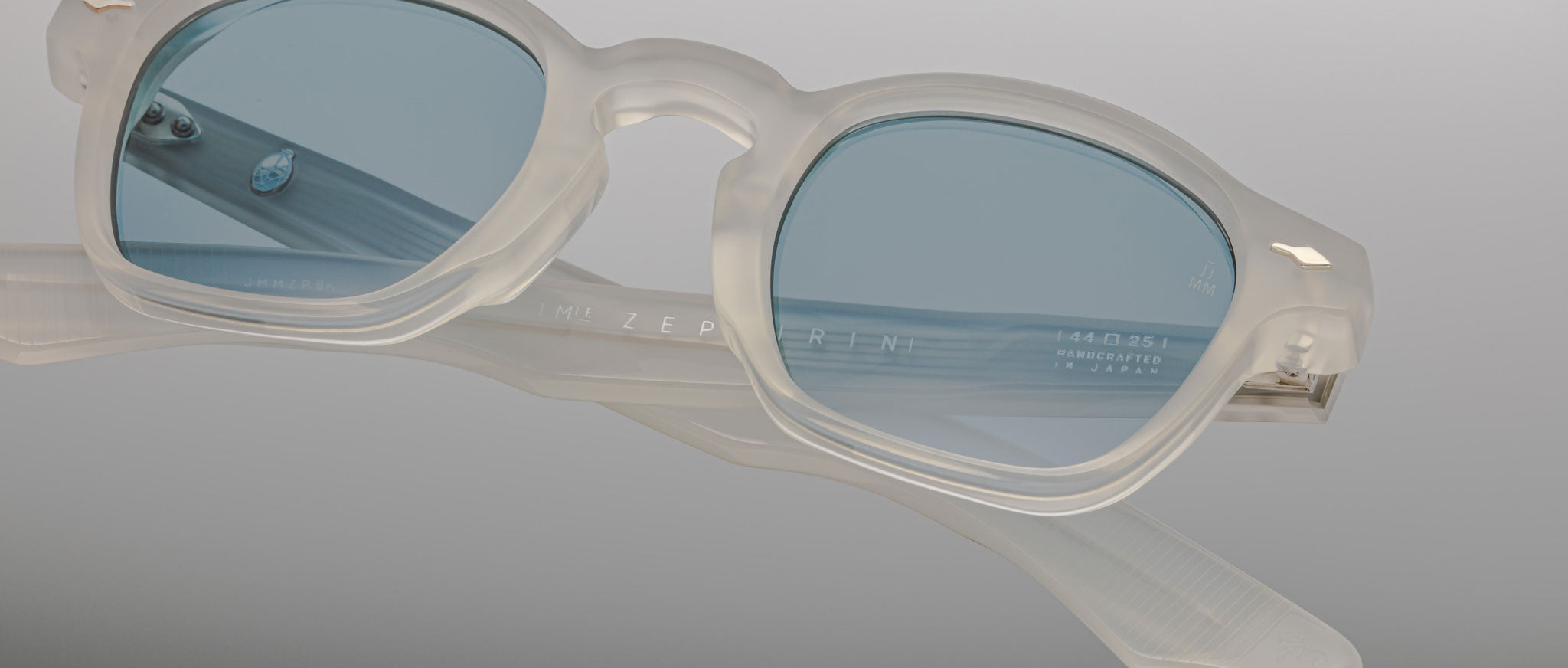 Jacques Marie Mage Zephirin eyeglasses feature translucent white acetate frames and blue-tinted rectangular lenses, presented on a grey gradient background.