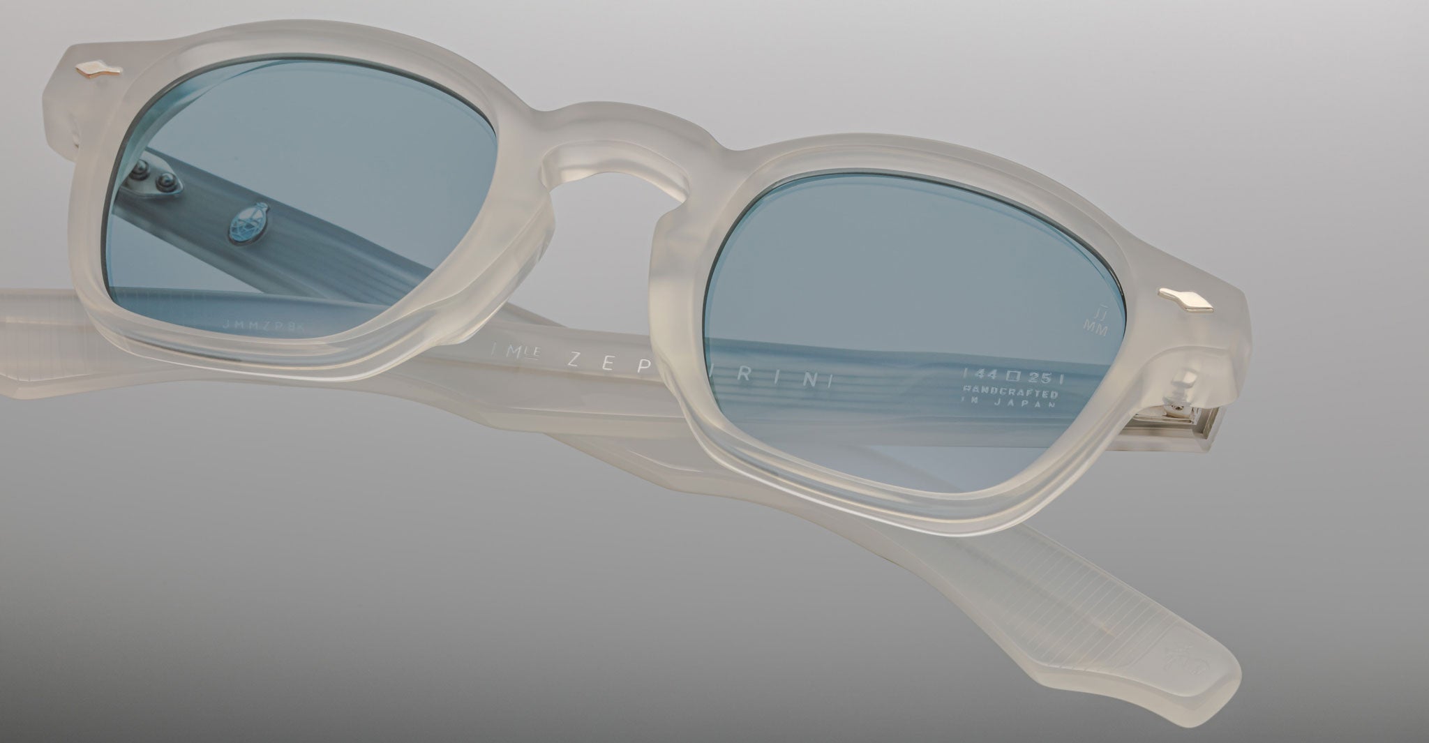 Jacques Marie Mage Zephirin eyeglasses feature translucent white acetate frames and blue-tinted rectangular lenses, presented on a grey gradient background.