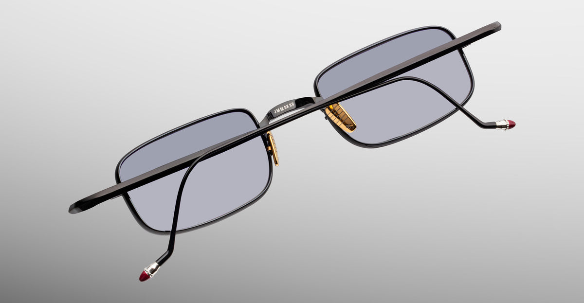 Jacques Marie Mage Dusk sunglasses with black frame, gold nose pads, and red arm tips shown from side angle.