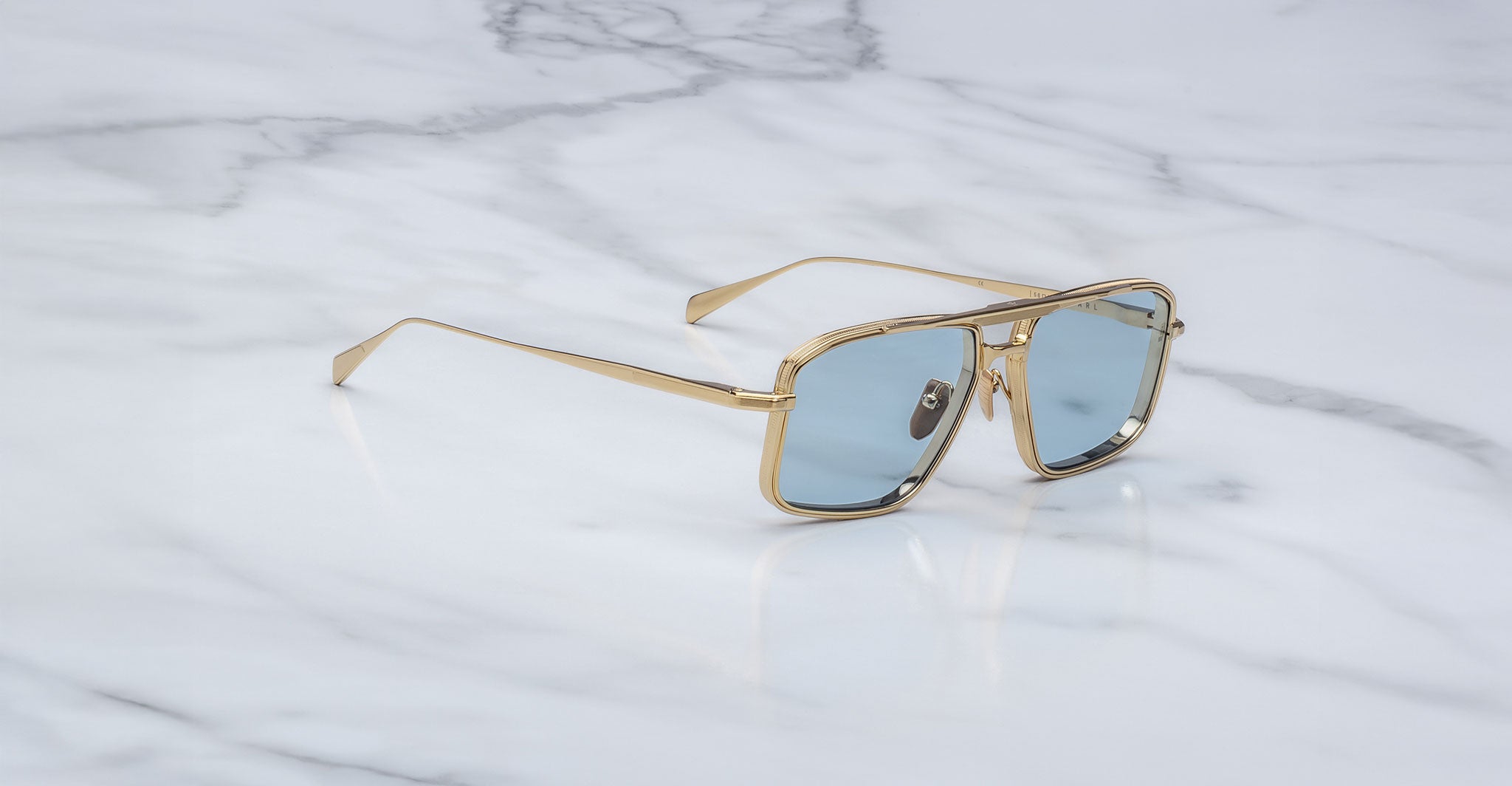Jacques Marie Mage Earl sunglasses with gold frames and blue-tinted lenses, top view.