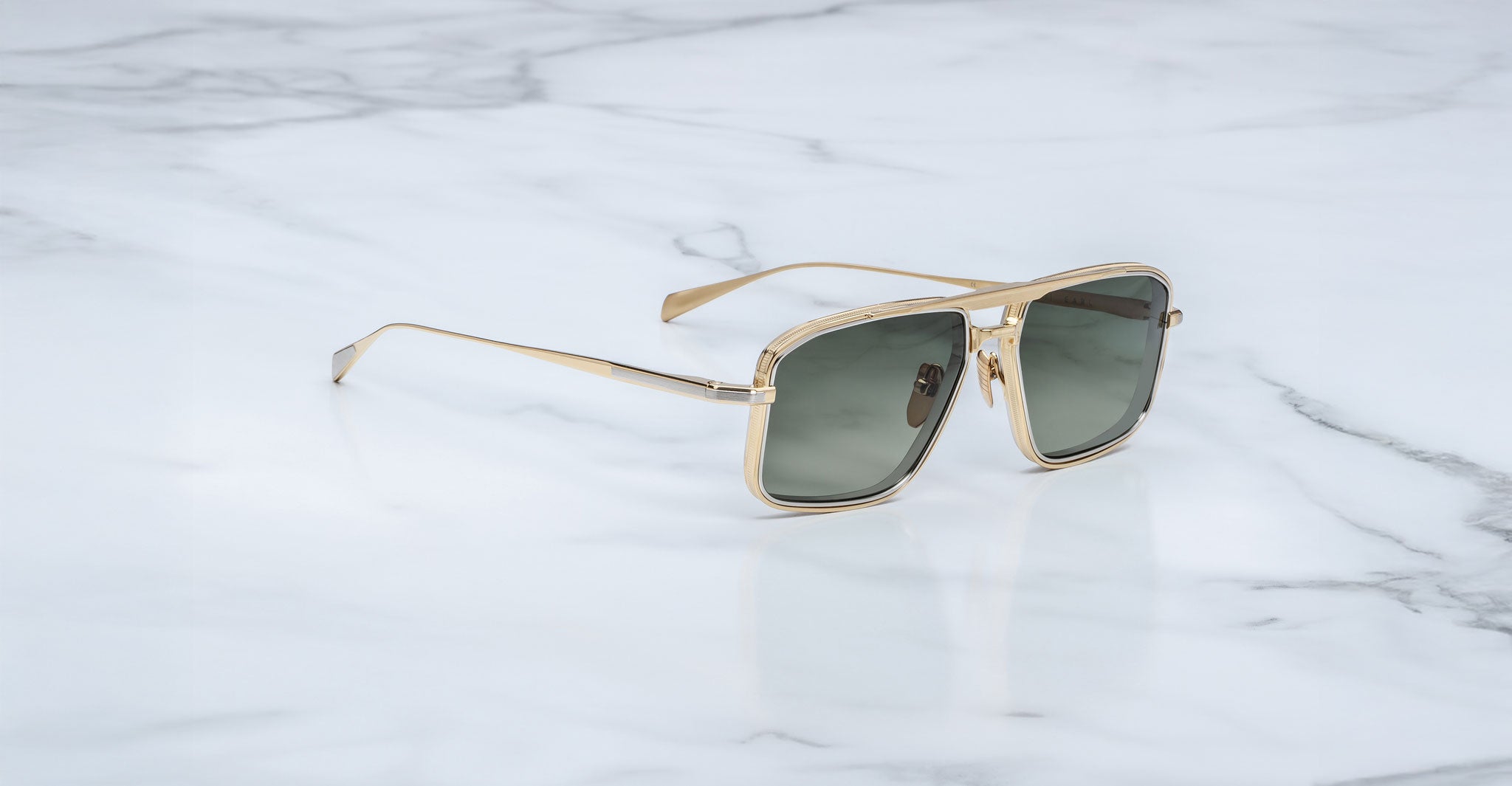 Jacques Marie Mage Earl gold-framed aviator sunglasses with dark lenses are displayed on a white marble surface with subtle grey veining.