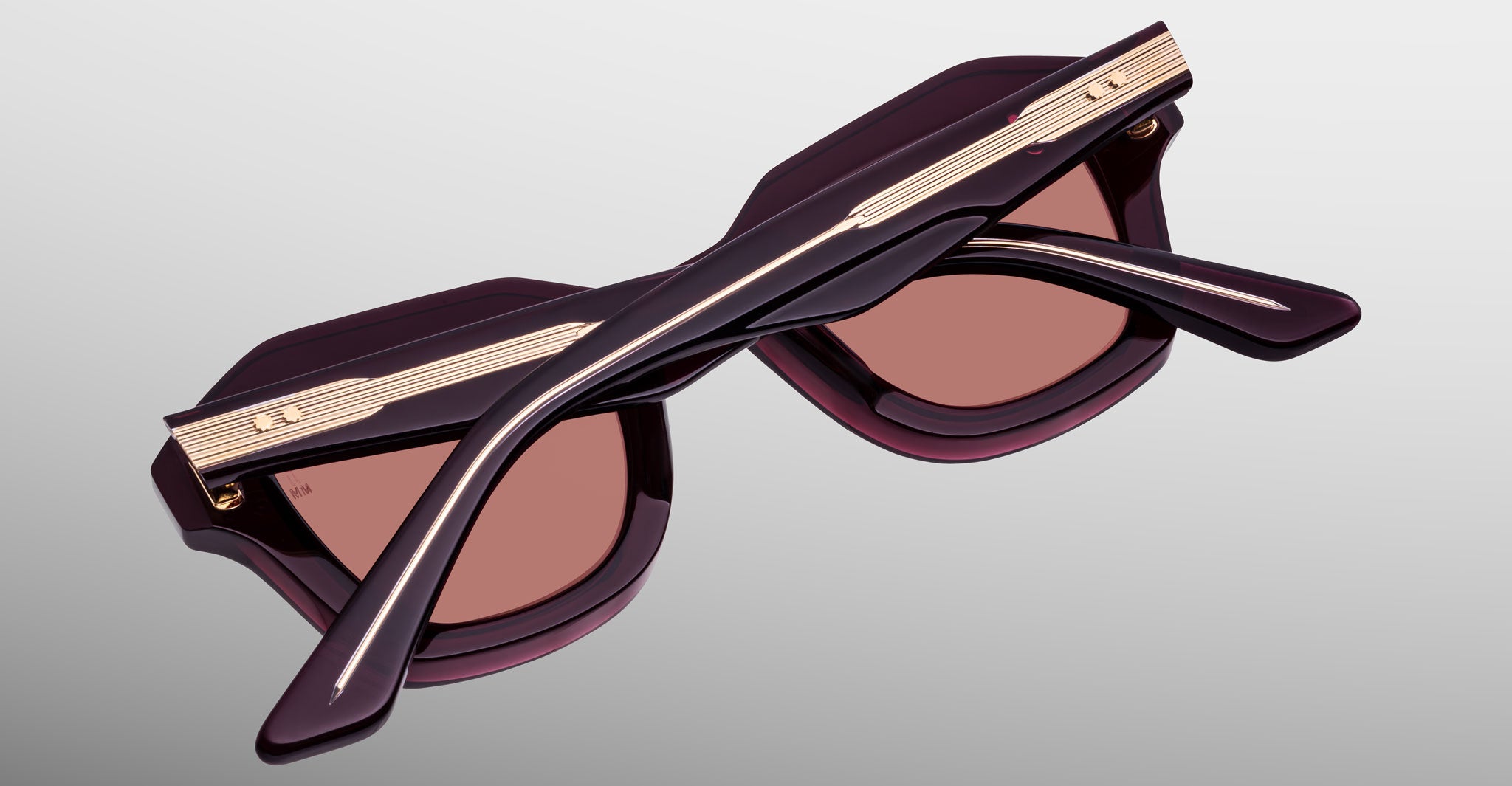 A pair of Jacques Marie Mage Eichler folded sunglasses with dark purple frames, brown lenses, and gold detailing on the temples is displayed against a light gray background.