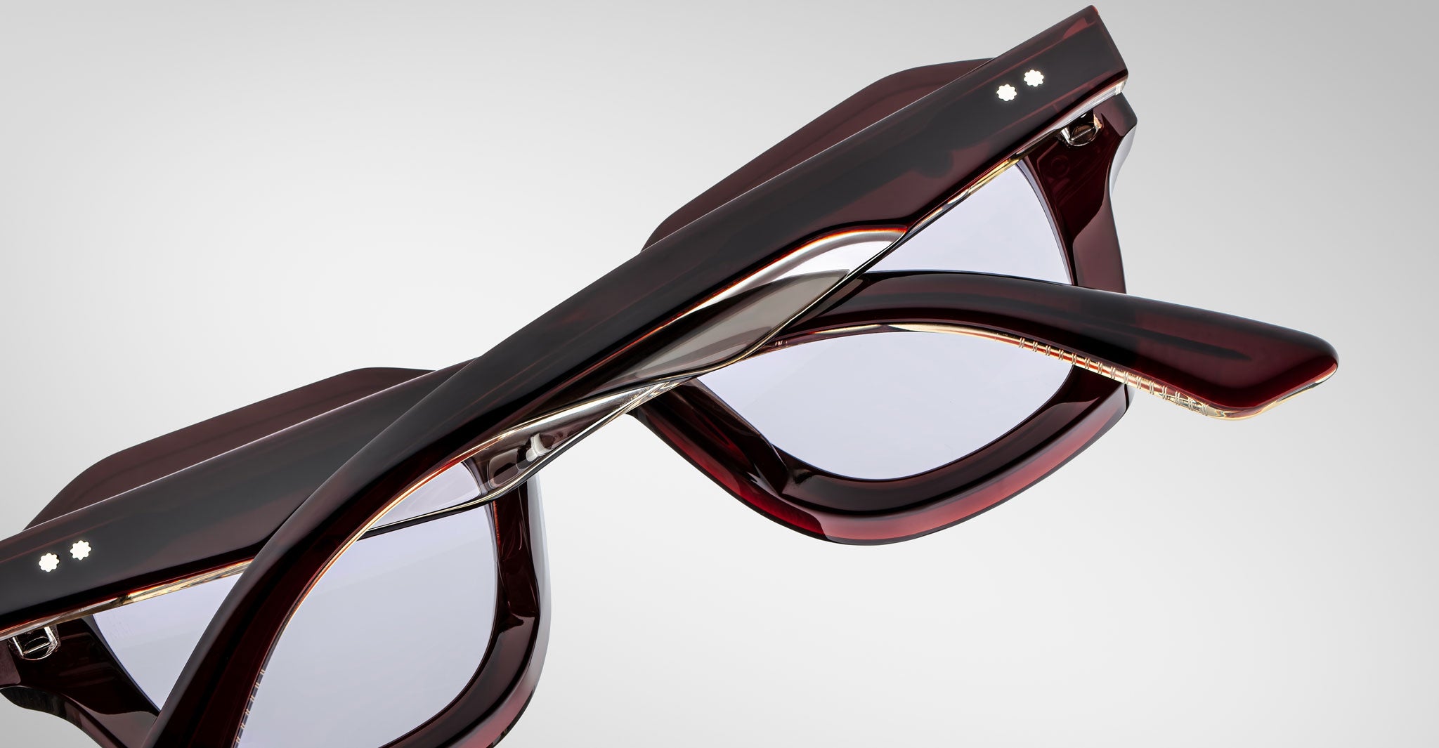 Detailed back view of a pair of Jacques Marie Mage Eichler cherry color, thick-framed sunglasses with lilac lenses on a plain background