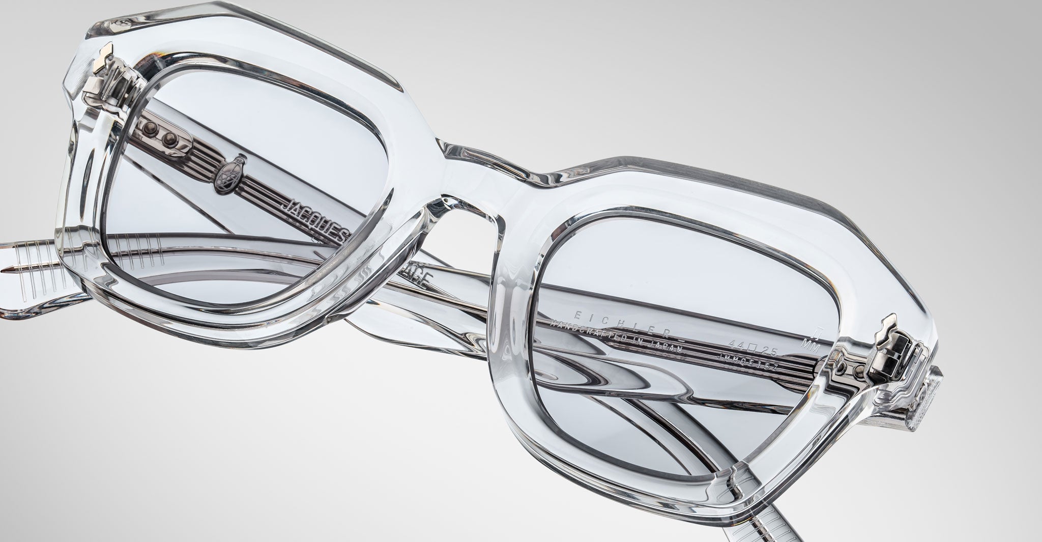 Detailed front view of a pair of Jacques Marie Mage Eichler crystal, thick-framed sunglasses with light grey lenses on a plain background