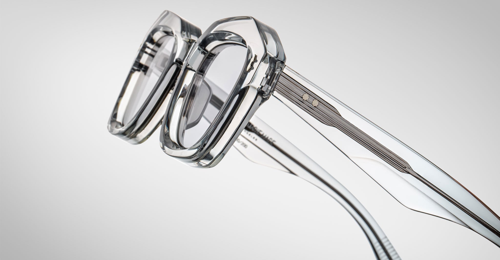 Detailed profile view of a pair of Jacques Marie Mage Eichler crystal, thick-framed sunglasses with light grey lenses on a plain background