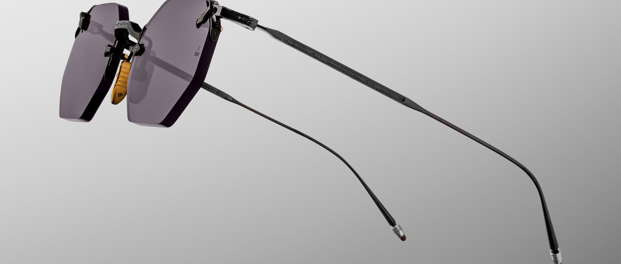 The Jacques Marie Mage El Dorado sunglasses feature a rimless design, dark tinted lenses, thin black metal temples, and nose pads, displayed against a plain gray background.