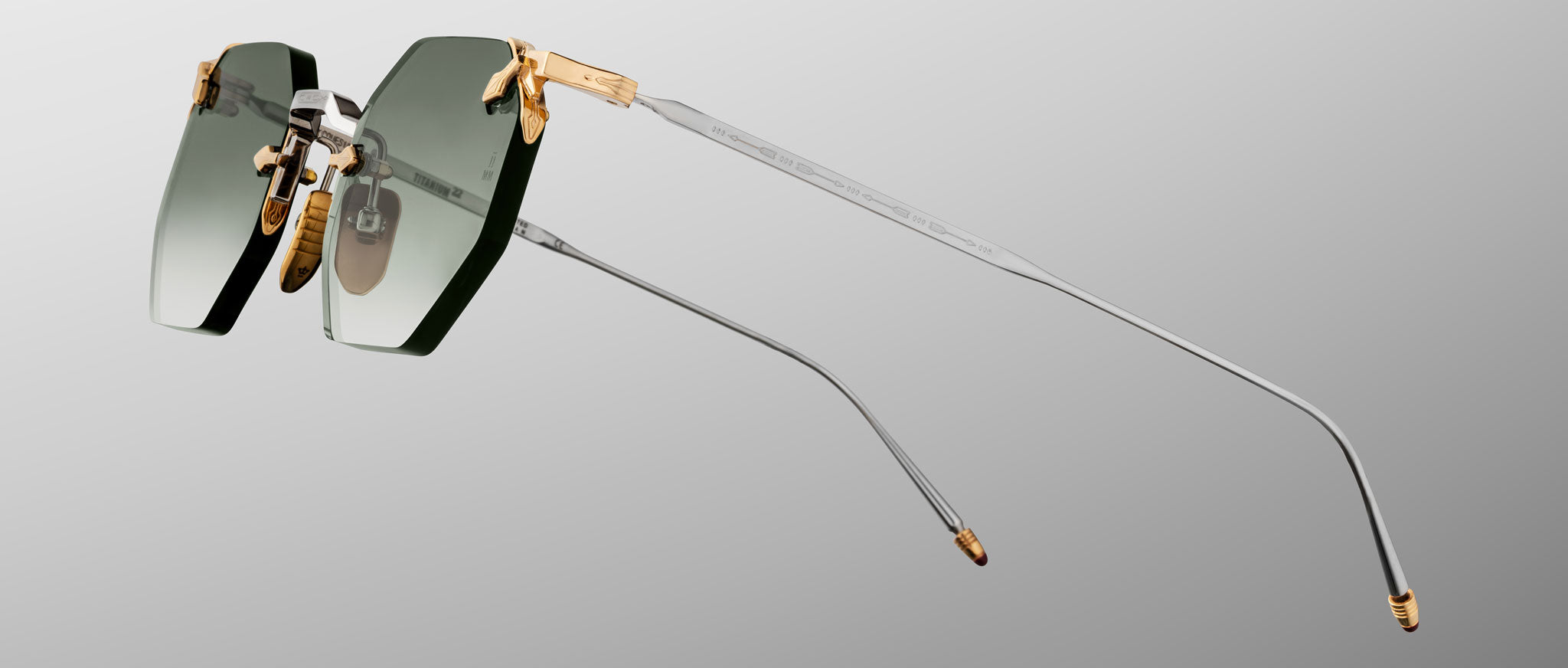 The Jacques Marie Mage El Dorado features rimless sunglasses with rectangular green-tinted lenses, gold accents at the hinges and nose bridge, and thin silver metal arms, shown against a gray gradient background.