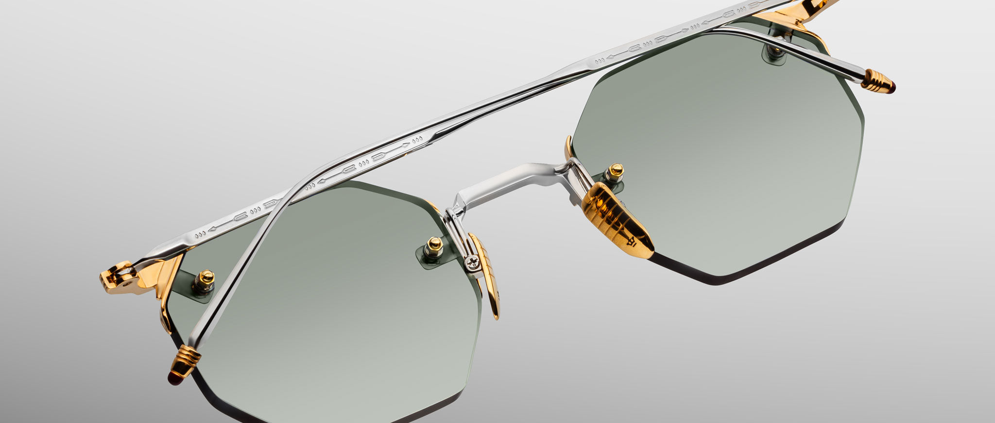 The Jacques Marie Mage El Dorado sunglasses feature geometric hexagonal frames in silver and gold metal, green-tinted lenses, and gold accents on the nose bridge and hinges, shown against a light gray background.