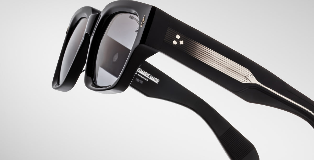 Close-up of Jacques Marie Mage Enzo black sunglasses showing metallic accents, grey lenses, and star motif on the temple.
