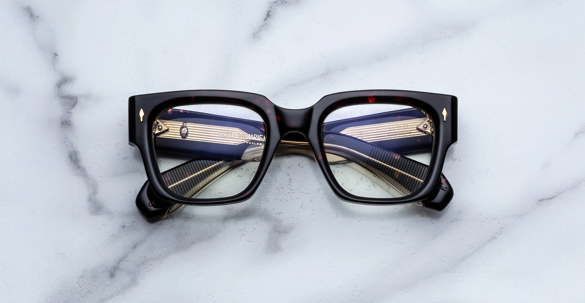 Jacques Marie Mage Enzo eyeglasses, thick black rims, blue and gold striped temples, front-facing view.