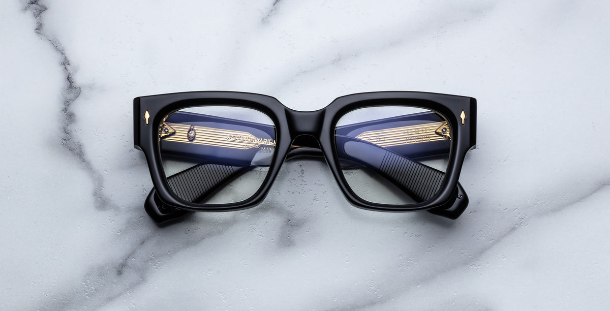 Jacques Marie Mage Enzo black rectangular eyeglasses with gold temples, top-down view.