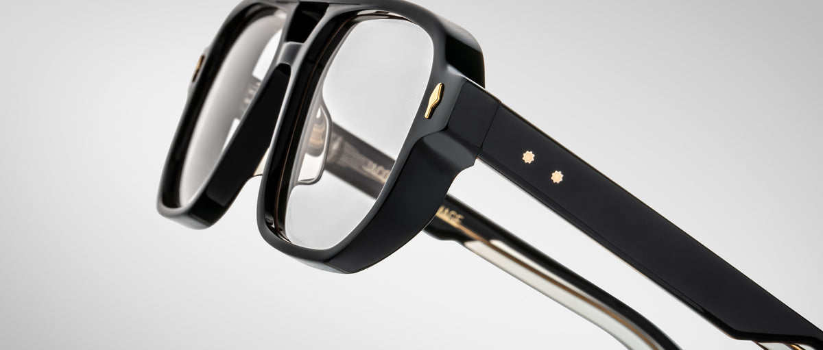 Close-up of the Jacques Marie Mage Evans glasses, showcasing black oversized acetate frames with gold accents and clear lenses against a plain light background.