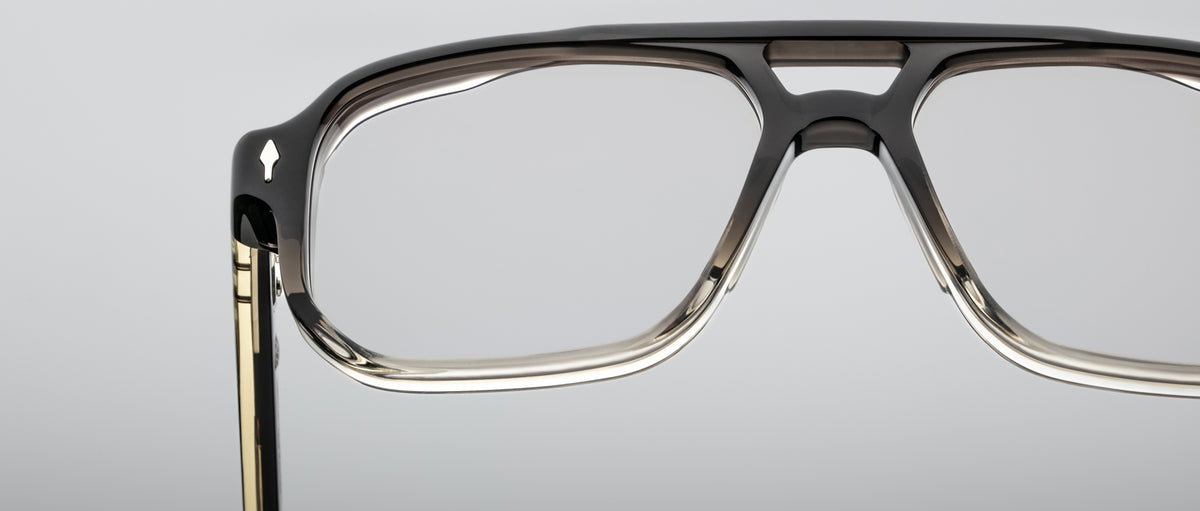 Close-up of the upper half of Jacques Marie Mage Evans optical glasses, showcasing an oversized handcrafted acetate frame against a plain grey background.