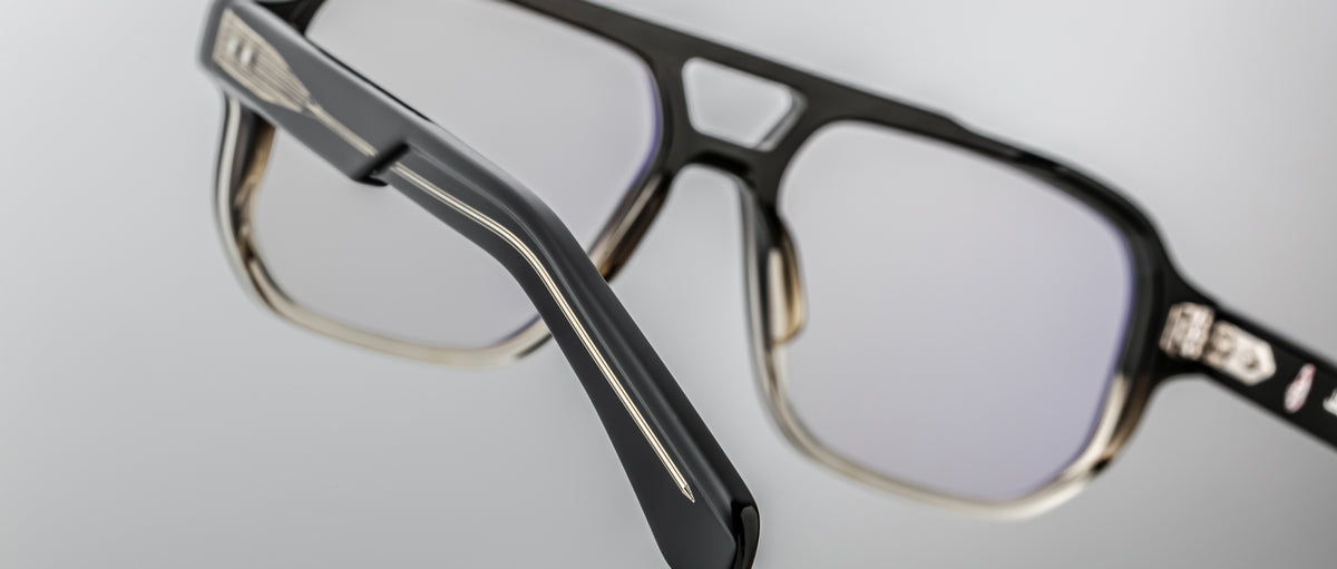 Close-up of Jacques Marie Mage Evans handcrafted black optical glasses with rectangular frames and clear lenses, highlighting temple and hinge details against a plain background.