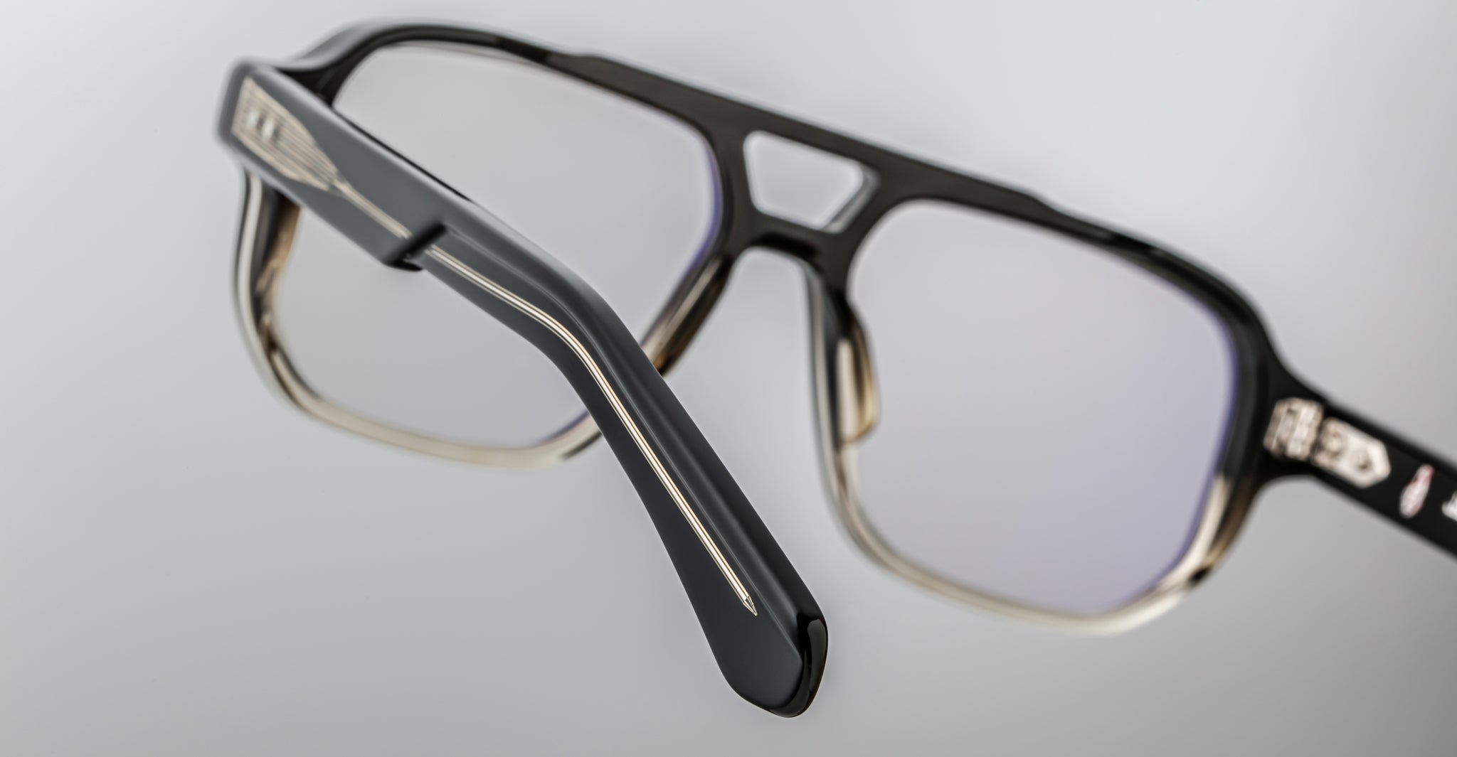 Close-up of Jacques Marie Mage Evans handcrafted black optical glasses with rectangular frames and clear lenses, highlighting temple and hinge details against a plain background.