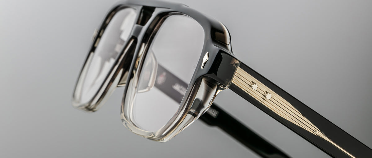 Close-up of the Jacques Marie Mage Evans optical glasses, handcrafted with an oversized black and clear acetate frame, gold accents, and decorative studs on the temples by Jacques Marie Mage, set against a neutral background.