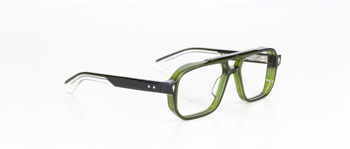 The Jacques Marie Mage Evans eyeglasses feature rectangular, thick-rimmed oversized acetate frames in translucent green and black, displayed on a white background.