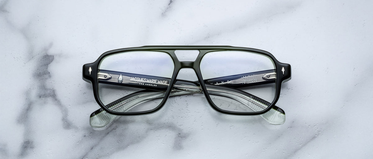The Jacques Marie Mage Evans are black, rectangular handcrafted optical glasses with clear lenses and an oversized acetate frame by Jacques Marie Mage, displayed on a white marble surface.