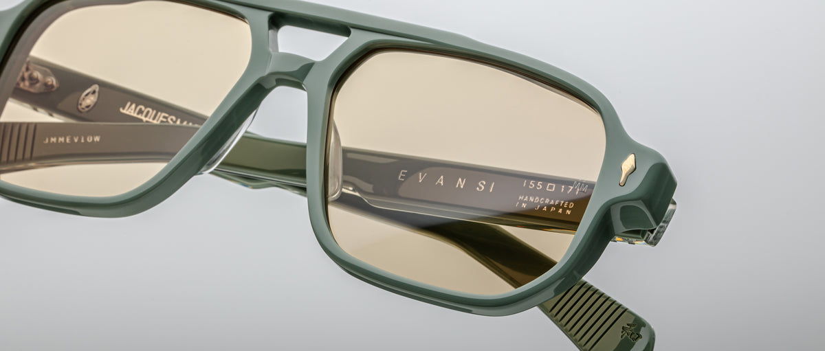 Close-up of green-framed Jacques Marie Mage Evans eyeglasses with tinted lenses, showcasing the brand name and model details engraved on the inner arms of these handcrafted optical glasses.