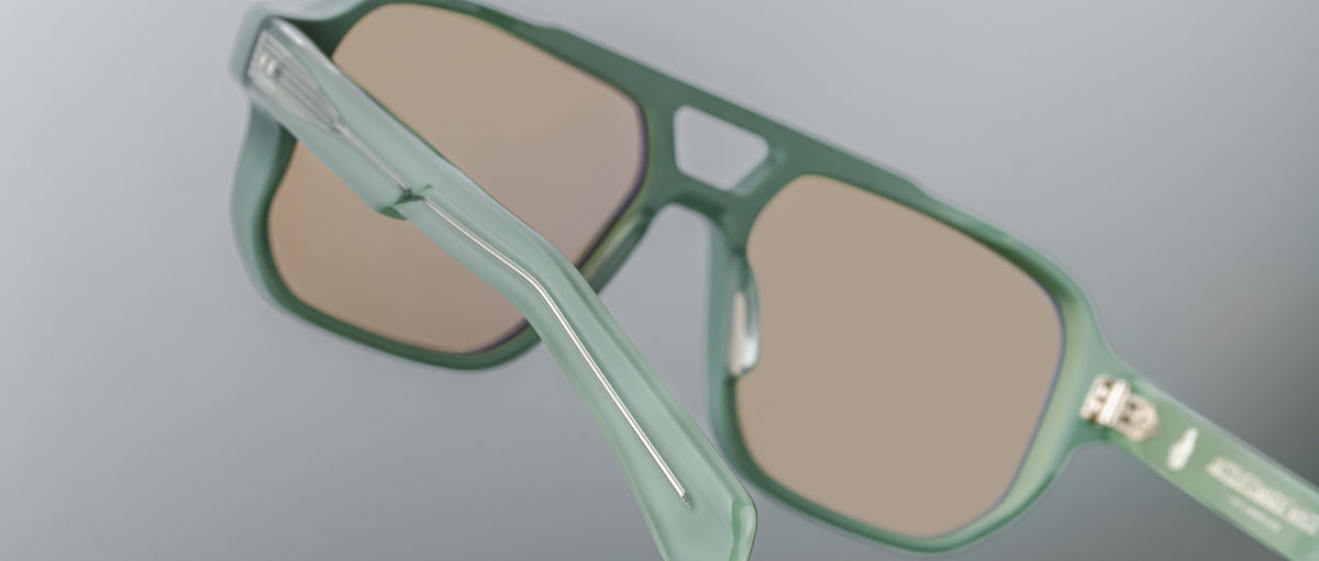 Close-up of the Jacques Marie Mage Evans: green oversized acetate sunglasses with brown-tinted lenses, highlighting the hinge and part of the temple arm—hallmarks of Jacques Marie Mage's unmistakable design.