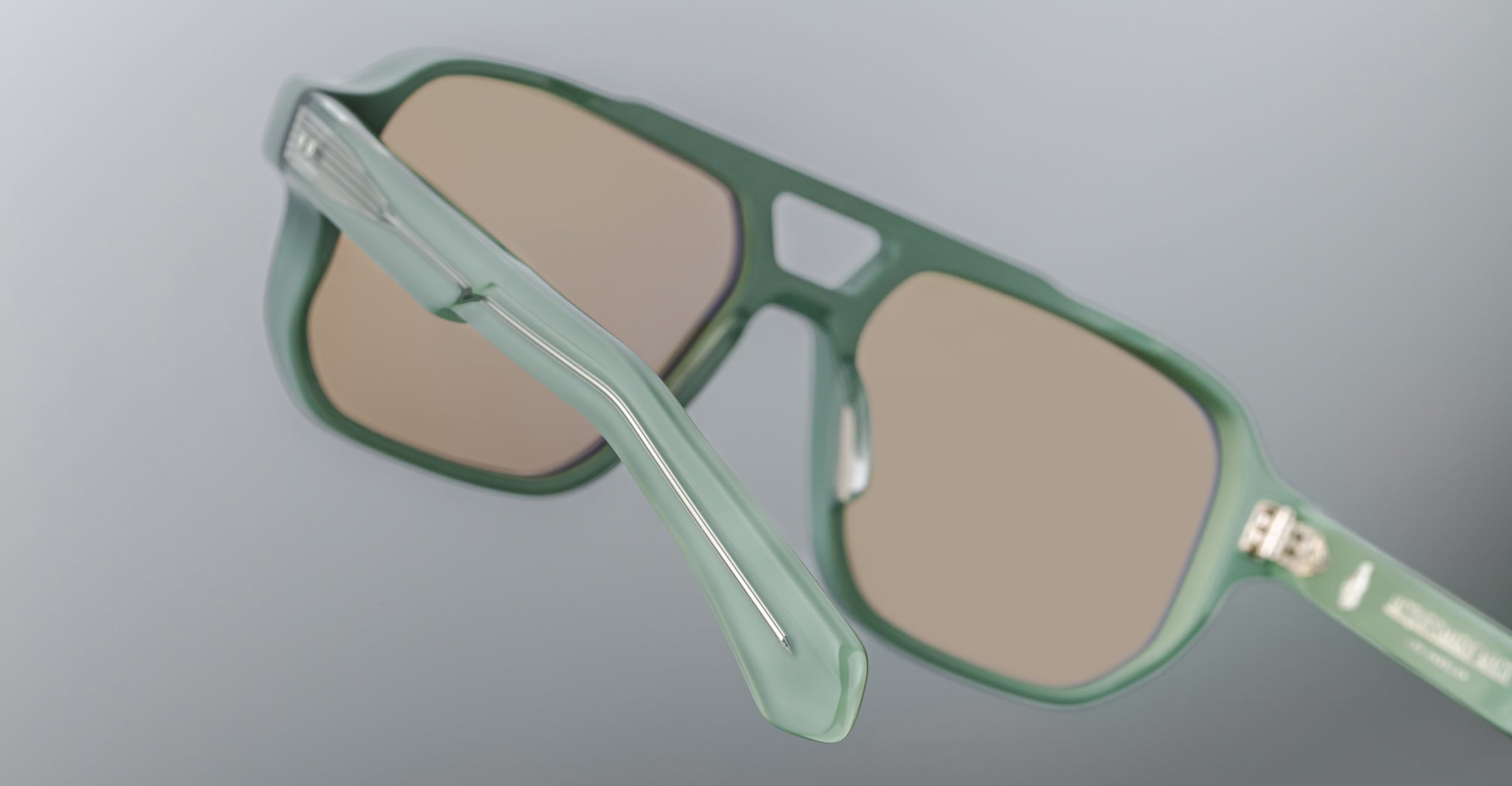 Close-up of the Jacques Marie Mage Evans: green oversized acetate sunglasses with brown-tinted lenses, highlighting the hinge and part of the temple arm—hallmarks of Jacques Marie Mage's unmistakable design.