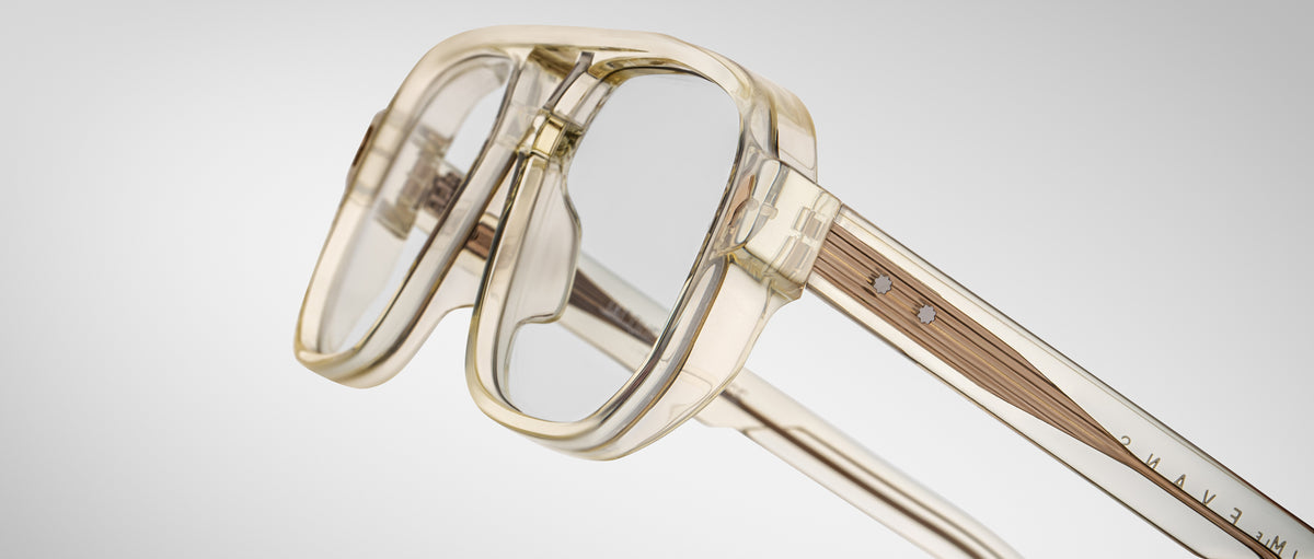 Close-up of Jacques Marie Mage Evans optical glasses, showcasing a thick oversized acetate frame, clear lenses, and metal temple accents against a plain light background.