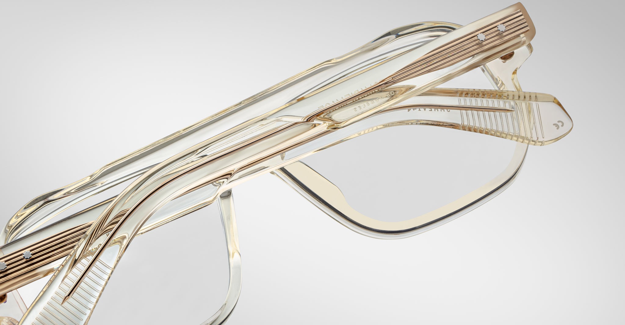 Close-up of two pairs of Jacques Marie Mage Evans optical glasses, featuring gold accents and oversized acetate frames, stacked on each other against a plain background.