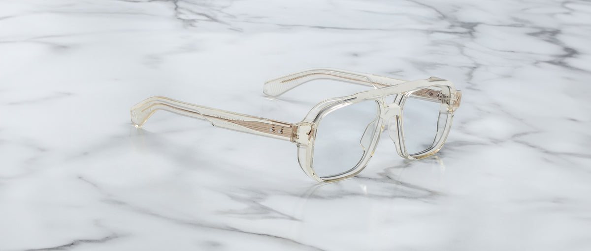 The Jacques Marie Mage Evans features clear, oversized acetate frames with rectangular lenses, elegantly displayed on a white marble surface.