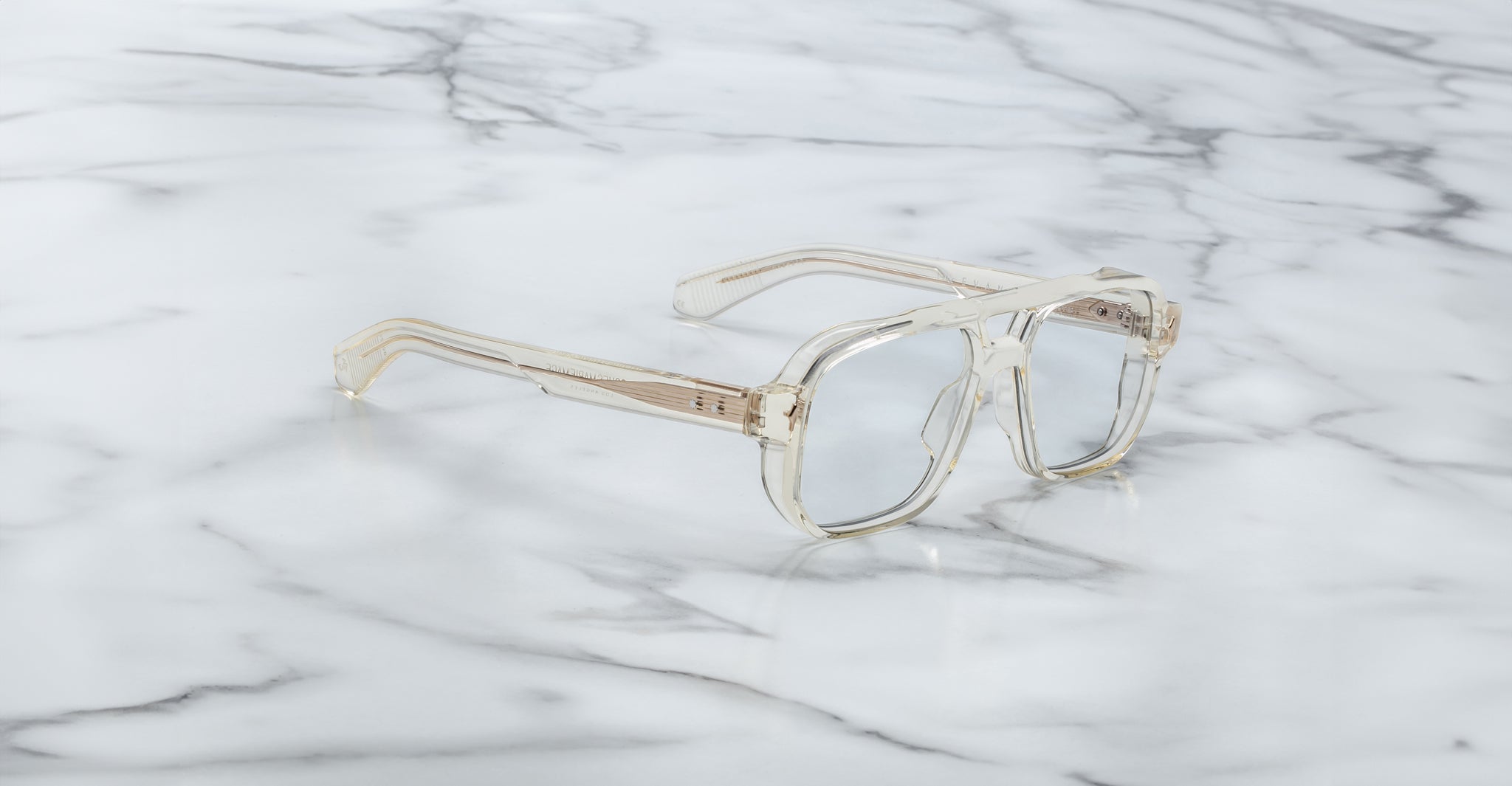 The Jacques Marie Mage Evans features clear, oversized acetate frames with rectangular lenses, elegantly displayed on a white marble surface.