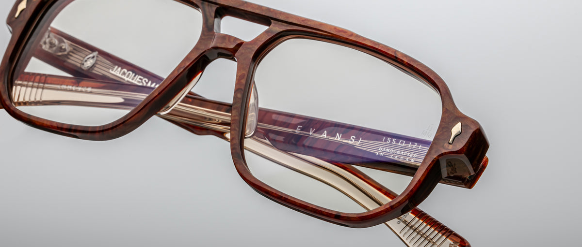 Close-up of Jacques Marie Mage Evans glasses, featuring a brown oversized rectangular acetate frame with brand markings on the temples, set against a plain light background.
