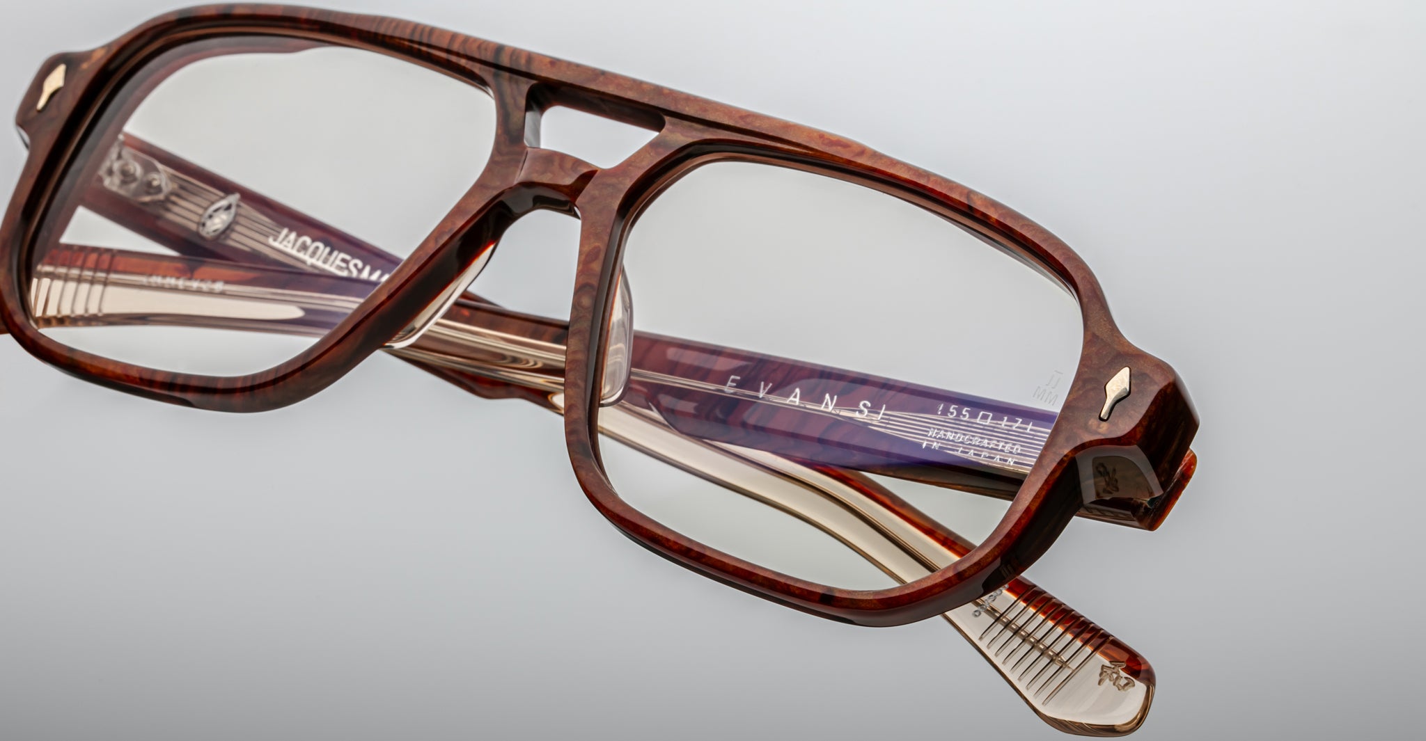Close-up of Jacques Marie Mage Evans glasses, featuring a brown oversized rectangular acetate frame with brand markings on the temples, set against a plain light background.