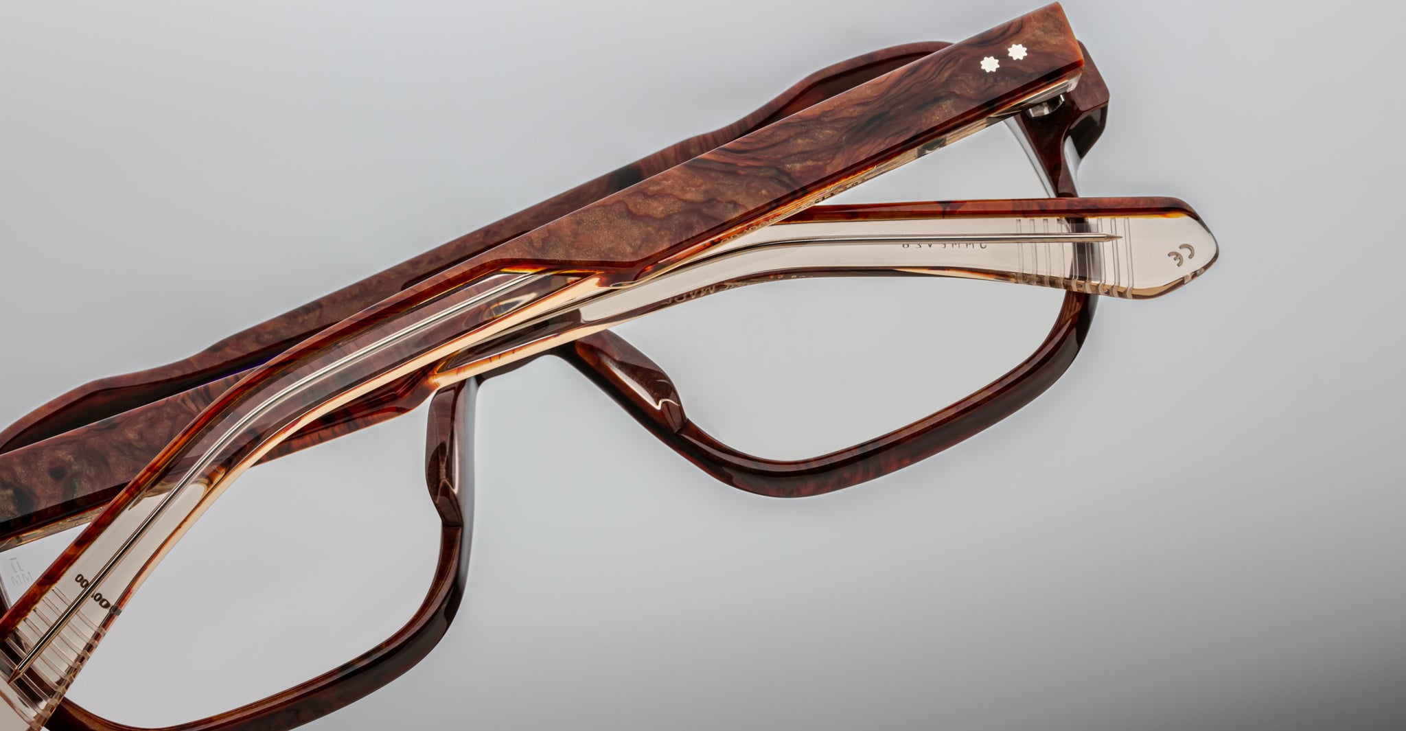 Two pairs of Jacques Marie Mage Evans optical glasses with brown tortoiseshell oversized acetate frames are stacked atop each other against a gray background.