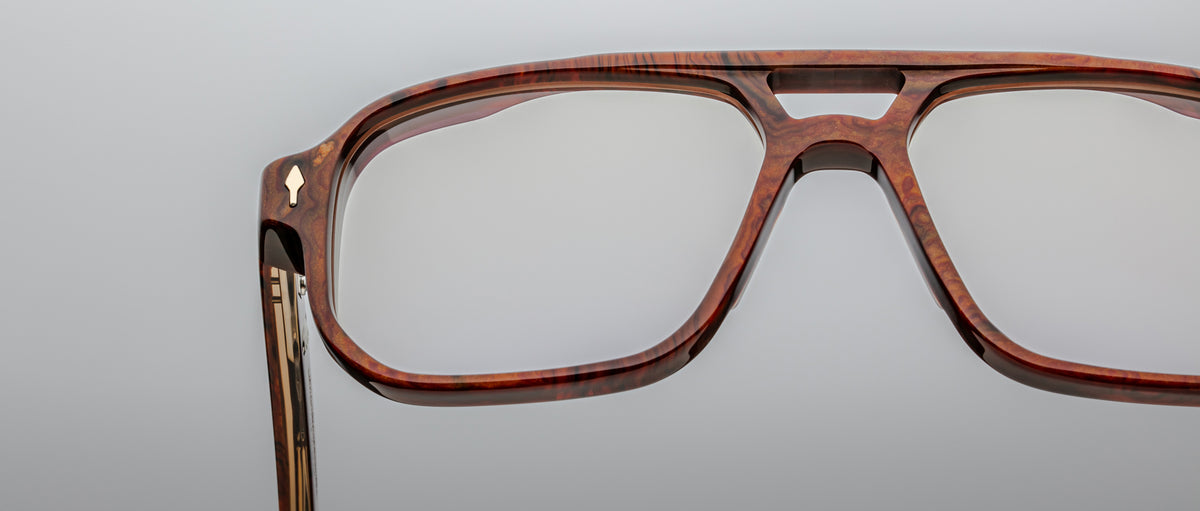 Close-up of handcrafted Jacques Marie Mage Evans optical glasses featuring large, brown, wood-patterned frames, set against a plain light gray background.