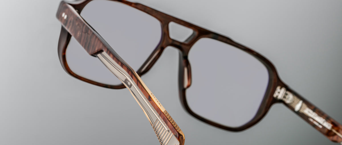 Close-up of Jacques Marie Mage Evans brown eyeglasses featuring clear lenses, an oversized acetate frame, and a detailed temple hinge, set against a gray background.