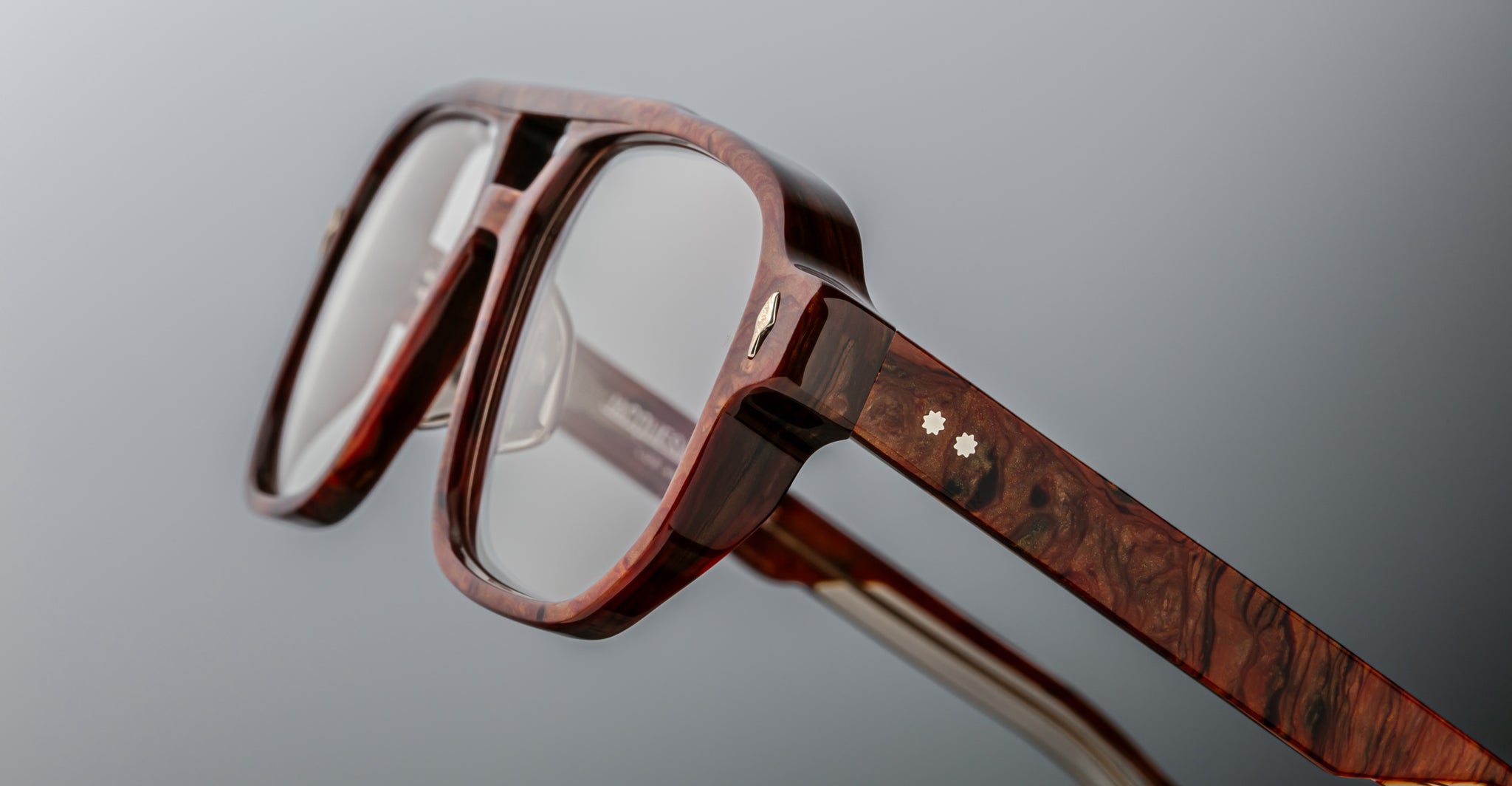 Close-up of Jacques Marie Mage Evans optical glasses, featuring thick wood-textured frames, transparent lenses, and small star-shaped inlays on the temple.