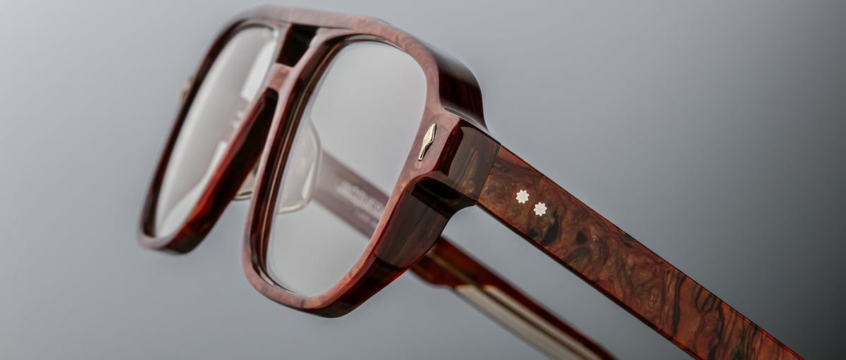 Close-up of Jacques Marie Mage Evans optical glasses, featuring thick wood-textured frames, transparent lenses, and small star-shaped inlays on the temple.