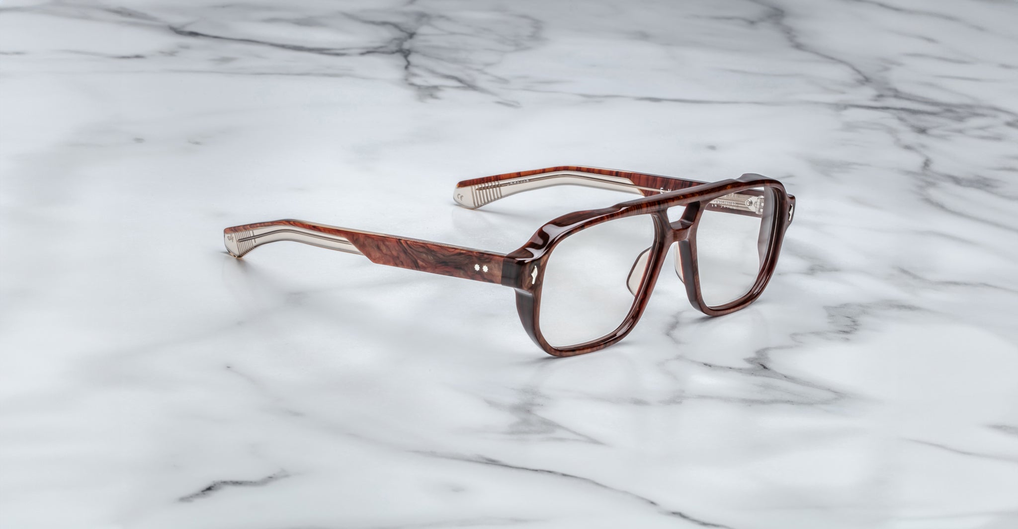 The Jacques Marie Mage Evans eyeglasses by Jacques Marie Mage feature an oversized brown acetate frame and clear lenses, displayed on a white marble surface to highlight their handcrafted optical design.