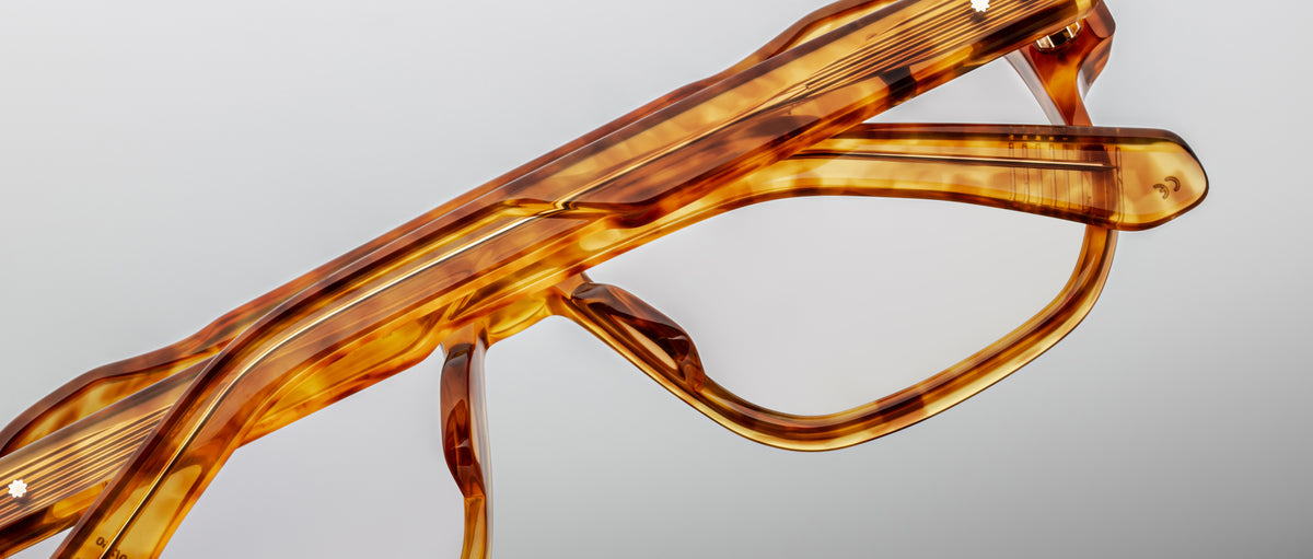 Close-up of the top half of Jacques Marie Mage Evans handcrafted optical glasses, showcasing an oversized brown acetate frame against a plain, light background.