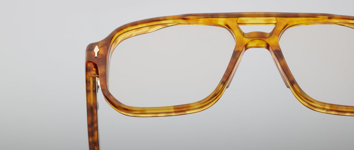 Close-up of Jacques Marie Mage Evans optical glasses, featuring amber tortoiseshell acetate with clear lenses in an oversized handcrafted frame, shown against a plain light background.