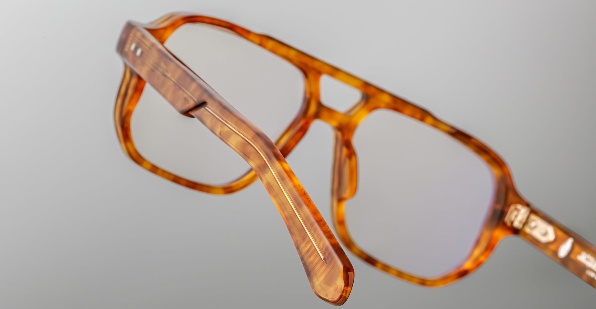 Close-up of Jacques Marie Mage Evans handcrafted optical glasses, featuring an oversized brown tortoiseshell acetate frame with clear lenses, showcasing detailed frame and temple design against a plain background.