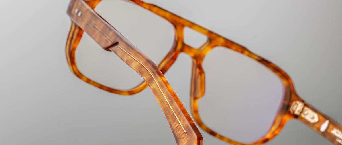Close-up of Jacques Marie Mage Evans handcrafted optical glasses, featuring an oversized brown tortoiseshell acetate frame with clear lenses, showcasing detailed frame and temple design against a plain background.