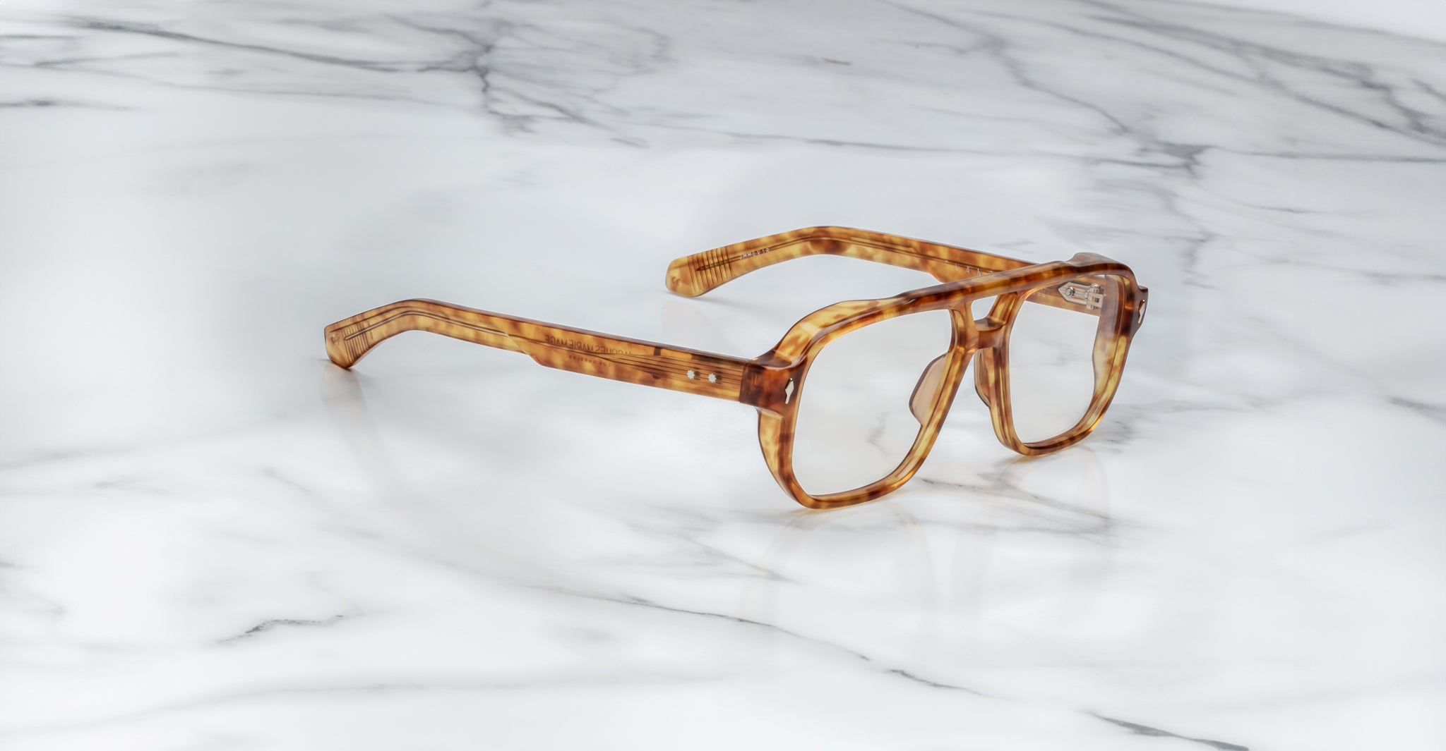 Jacques Marie Mage Evans oversized acetate eyeglasses in brown tortoiseshell by Jacques Marie Mage are displayed on a white marble surface, highlighting their handcrafted optical style.