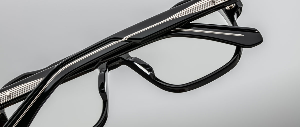 Close-up of Jacques Marie Mage Evans handcrafted optical glasses featuring silver detailing and an oversized acetate frame, displayed against a plain gray background.